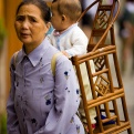 A Chinese grandmother uses a traditional strapped wooden baby carrier, chair.